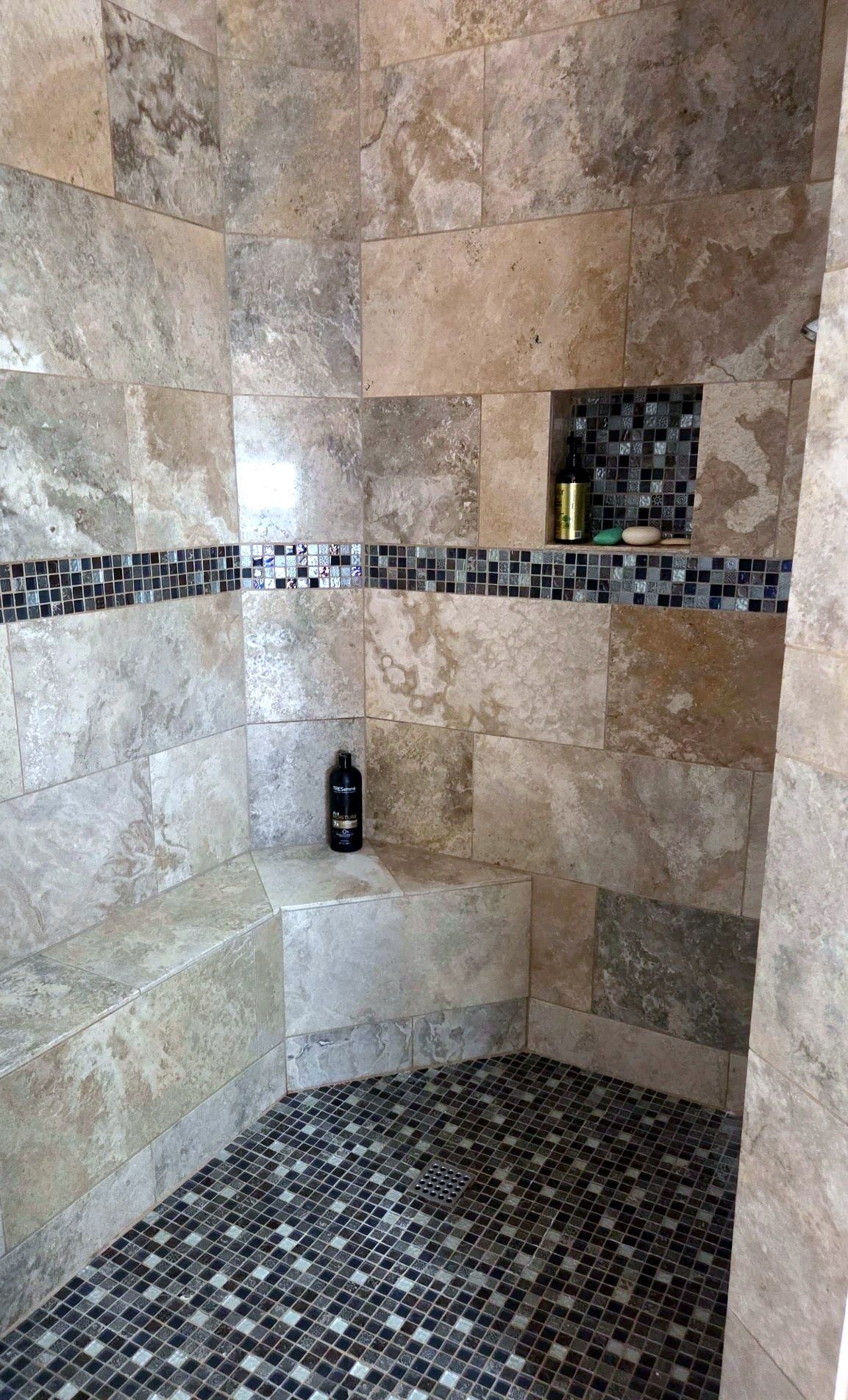 Walk-in shower with travertine walls and glass mosaic floor, cleaned